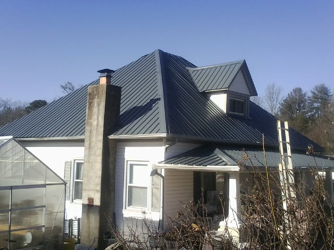 Dark blue standing seam metal roof on a white farmhouse with dormer — Slate & Tile Roof Repair by Roofing Brothers in Eastover