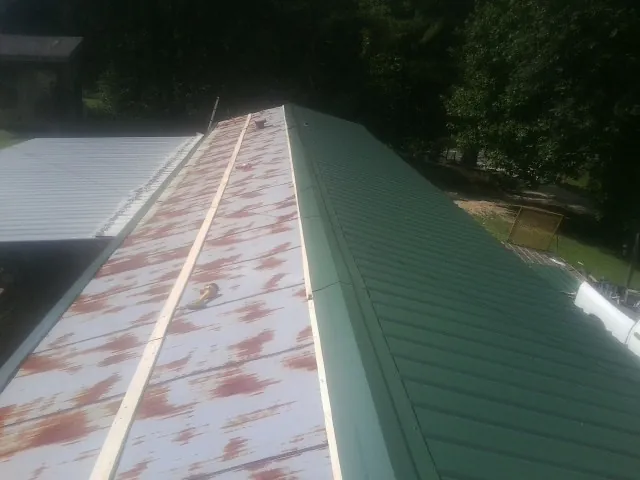 Old rusted panels beside newly installed green metal roofing — Wind Damage Roof Repair by Roofing Brothers in Eastover