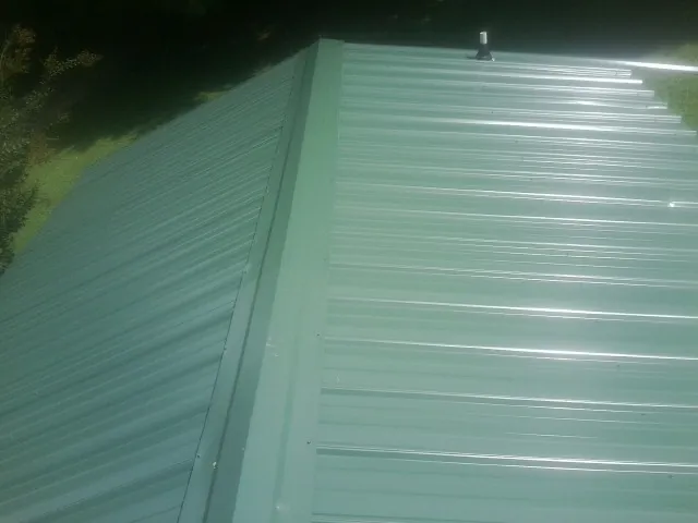 New green metal panels meeting at the ridge of a roof — Flat Roof Repair work by our crew in Eastover