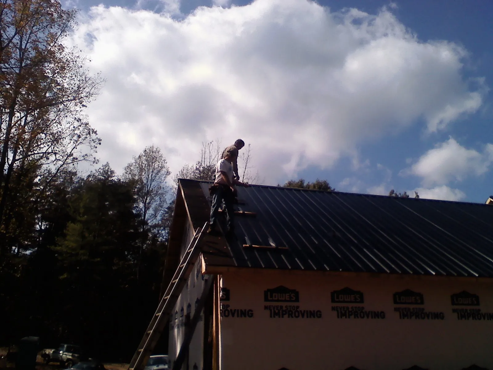 Roofer fastening dark metal panels high against a cloudy sky, from a Roof Inspection job in Eastover