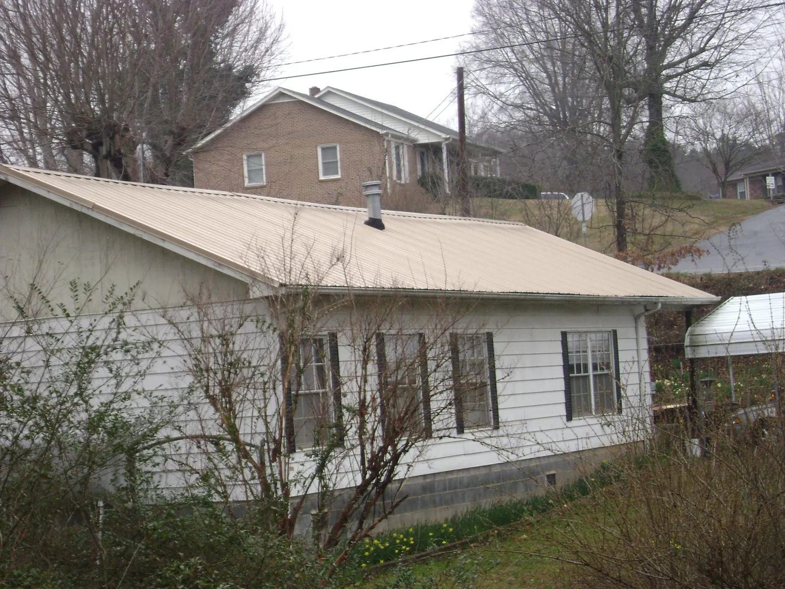 Tan metal roof on a white sided house set into a hillside — Commercial Roofing by Roofing Brothers in Eastover