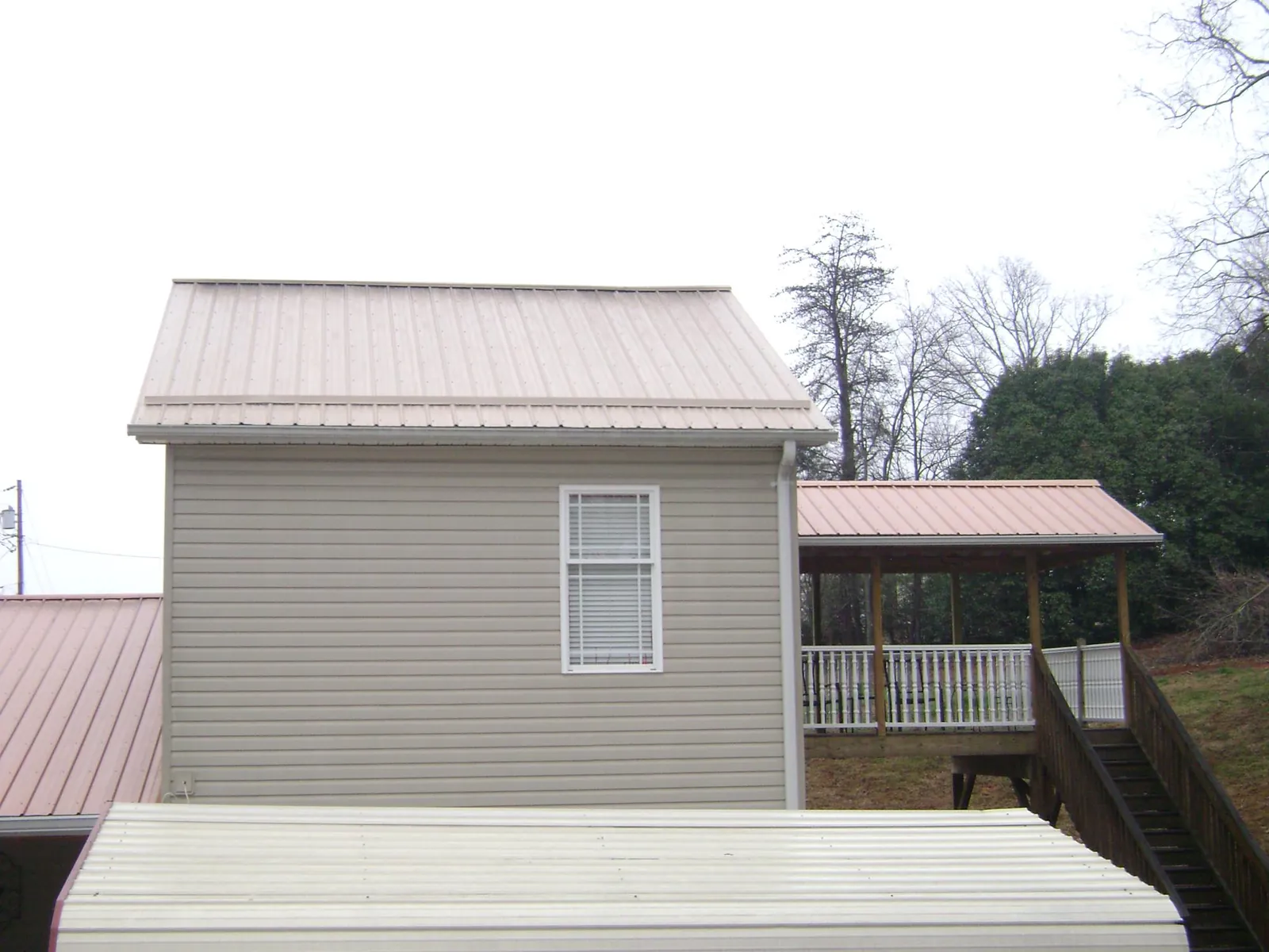 Tan metal roofs on a two story addition and attached porch, from a Roof Replacement job in Eastover
